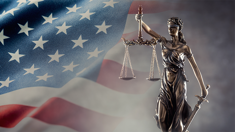 Justice is blind statue symbolizing law with scales and sword in hands and a US flag in the background