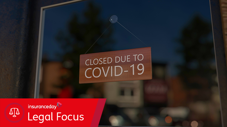 Close-up on a closed sign in the window of a shop displaying the message "Closed due to Covid-19". The glass reflects the day city  