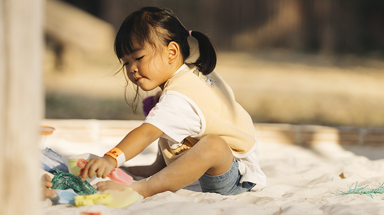 Concentrated young child playing with colorful sand toys on a sandy beach during a sunny day