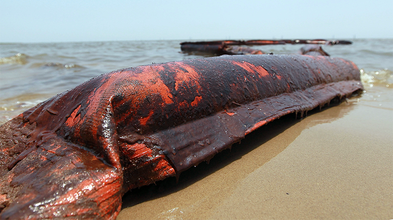 An oil-coated containment boom is seen on a beach