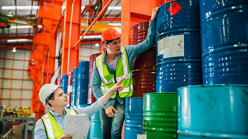 Industrial engineers inspect liquid storage drums in large-scale warehouse for export logistics.