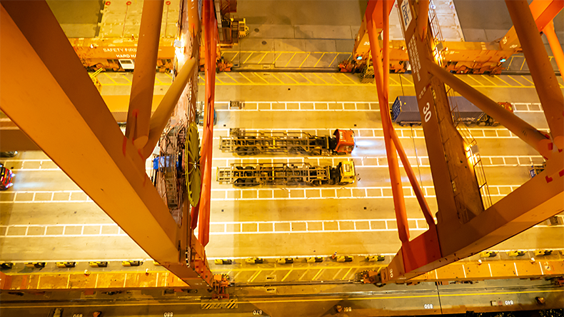 Container tracks between two gantry cranes on Shekou Container Terminal during the night, view from sky