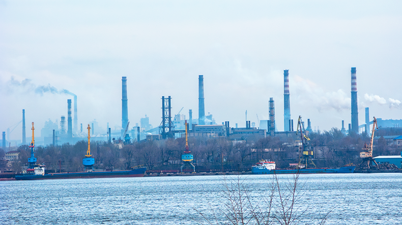 White smoke billowing out from factory tall pipes as seen across fright port on left bank of Dnipro river in industrial city of Zaporizhzhia, Ukraine
